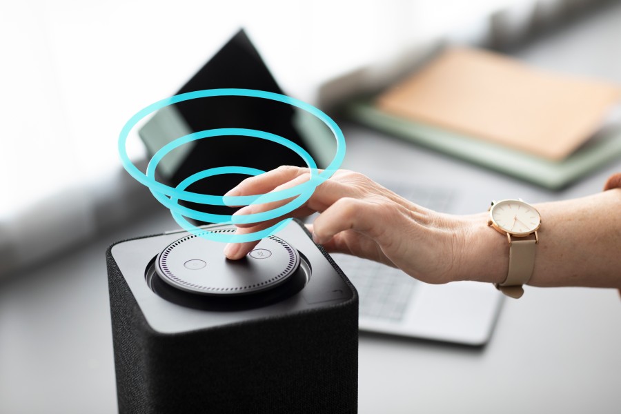 Hand touching a smart speaker with a glowing blue holographic interface above it.